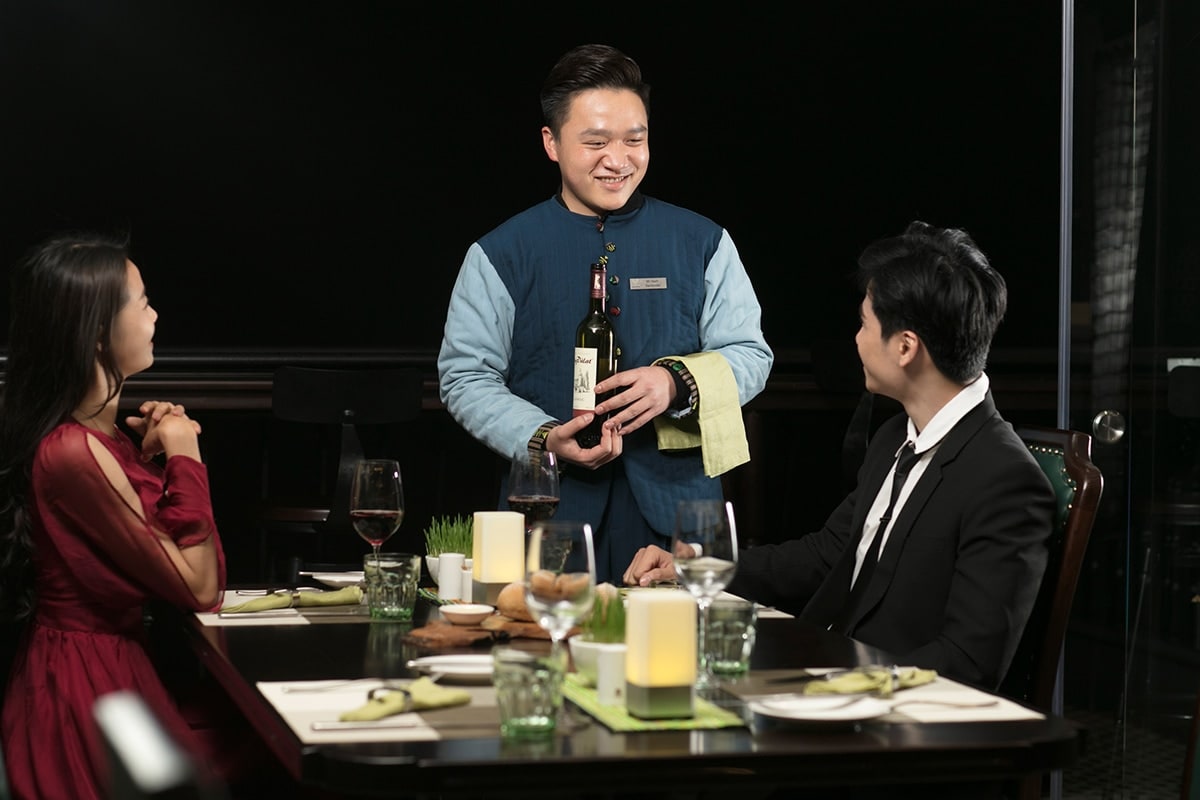 Staff member serving wine to a couple during dinner at the restaurant of DeLaSol Phat Linh Hotel Sapa